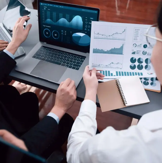 Two people looking over some graphs on paper and on a laptop